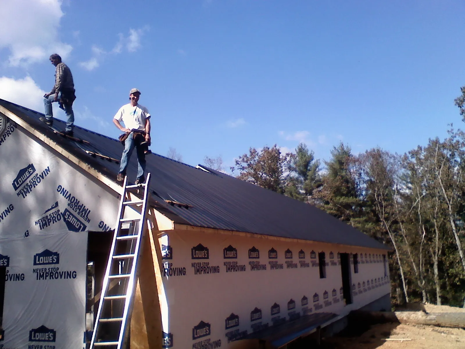 Two roofers standing on a long dark metal roof over a wrapped building in Rutland